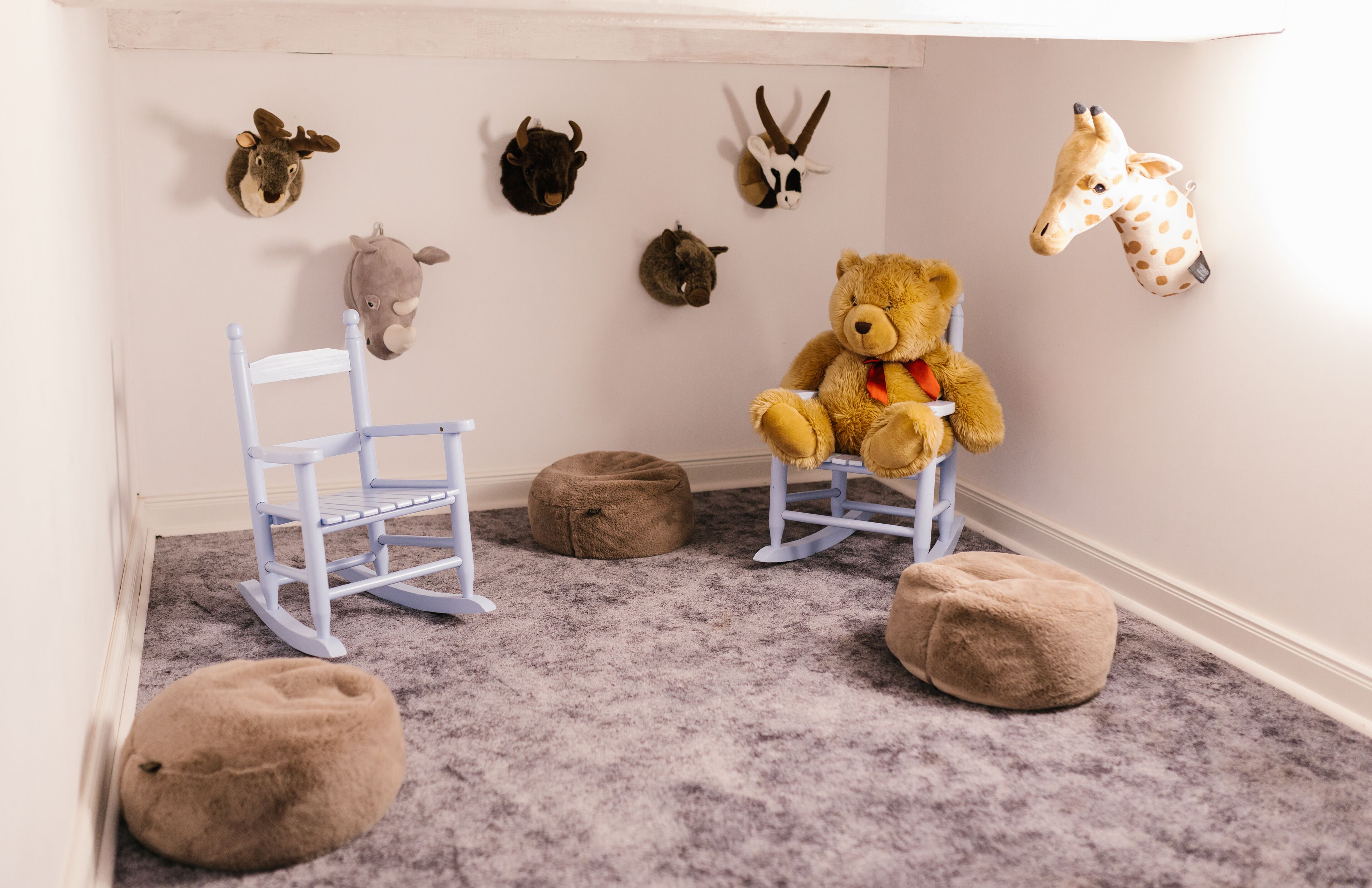 Une salle de jeux pour enfants avec un fauteuil à bascule, un pouf et des peluches.