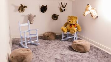 Une salle de jeux pour enfants avec un fauteuil à bascule, un pouf et des peluches.