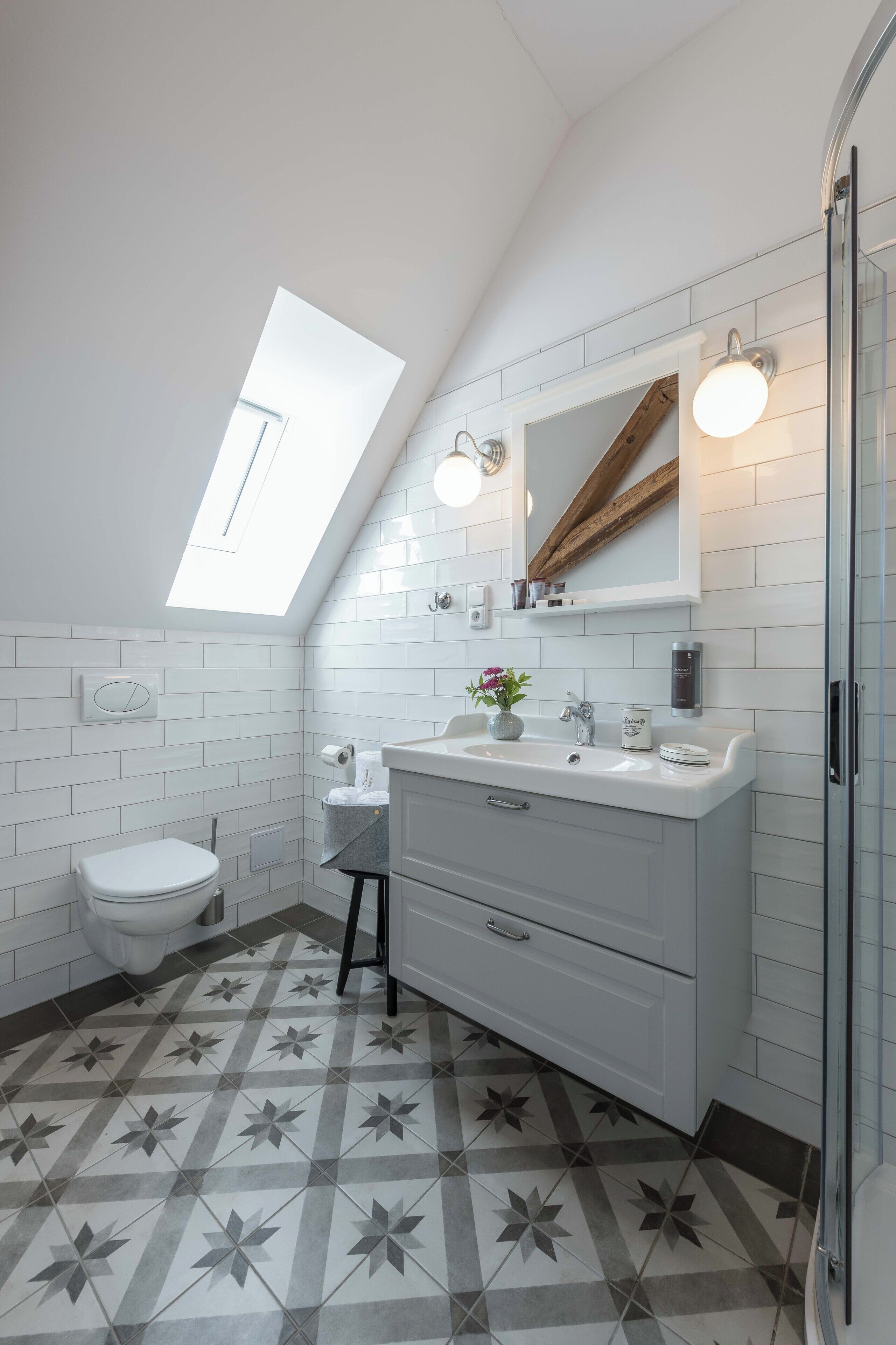 Un baño moderno con tragaluz, azulejos blancos, tocador con espejo y zona de ducha.