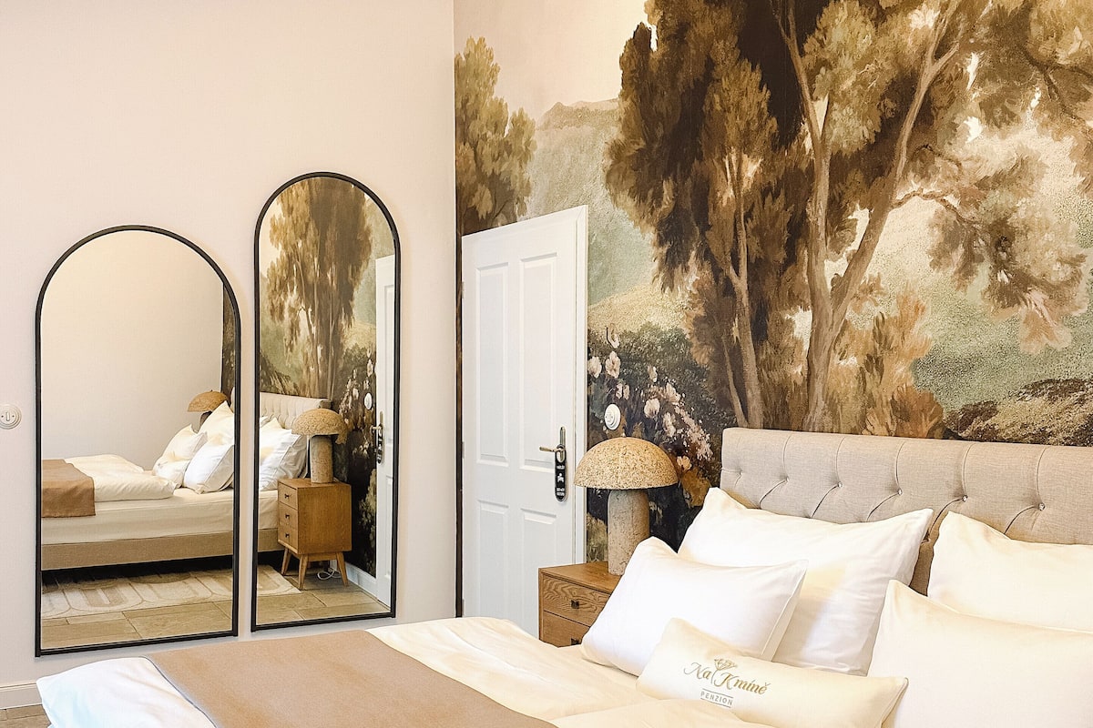 A bedroom with a large bed, two mirrors, a door, and a mural of trees.