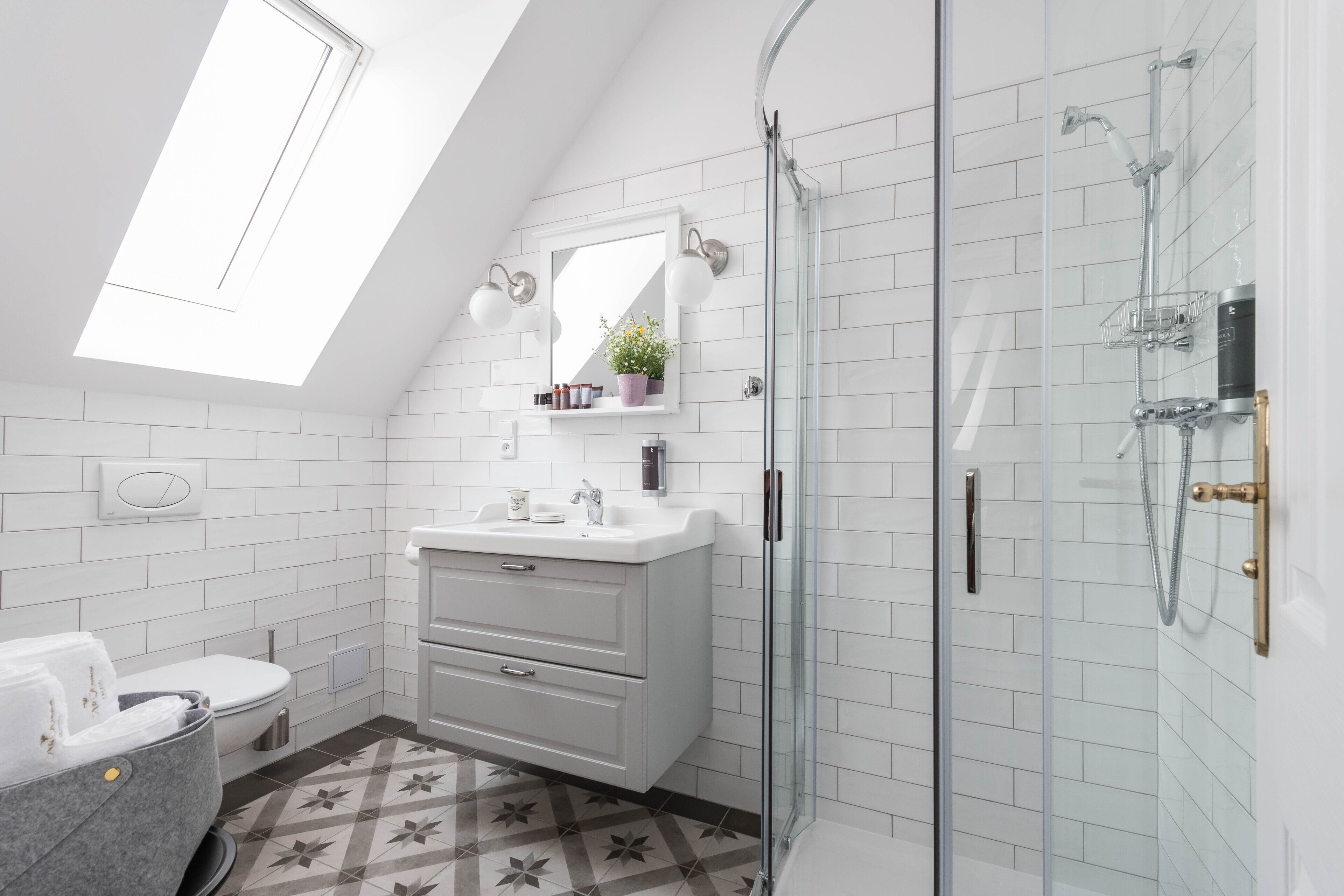 A modern bathroom with a skylight, a glass-enclosed shower, a white vanity, and a patterned floor.