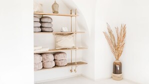 A minimalist interior with a wooden shelf unit holding various items, a vase with dried plants, and a white wall. - Na Kmíně (Obríství)