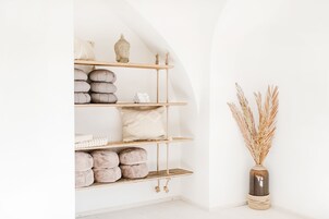 Un interior minimalista con una estantería de madera que alberga varios objetos, un florero con plantas secas y una pared blanca.