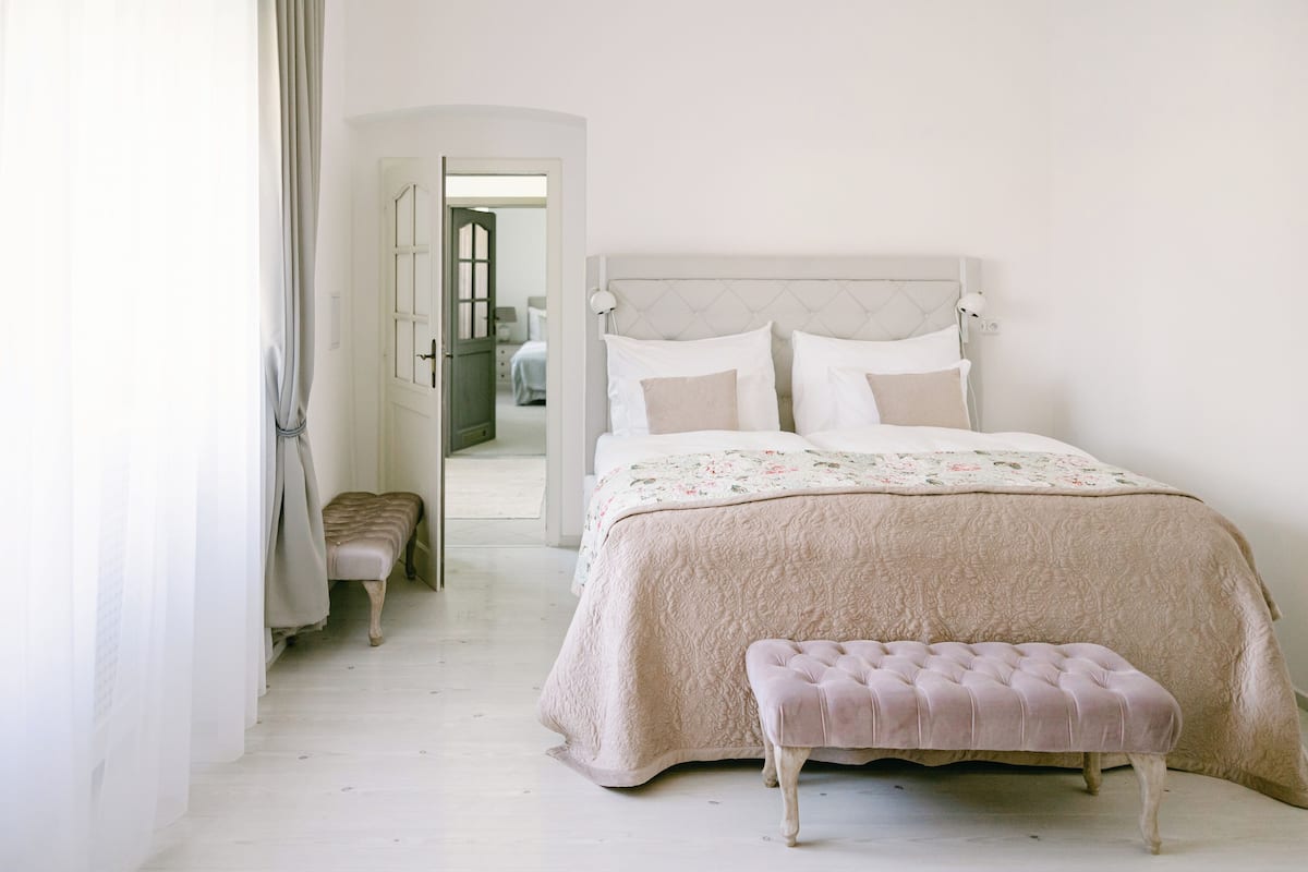 A bedroom with a bed, a bench, and a door leading to another room.