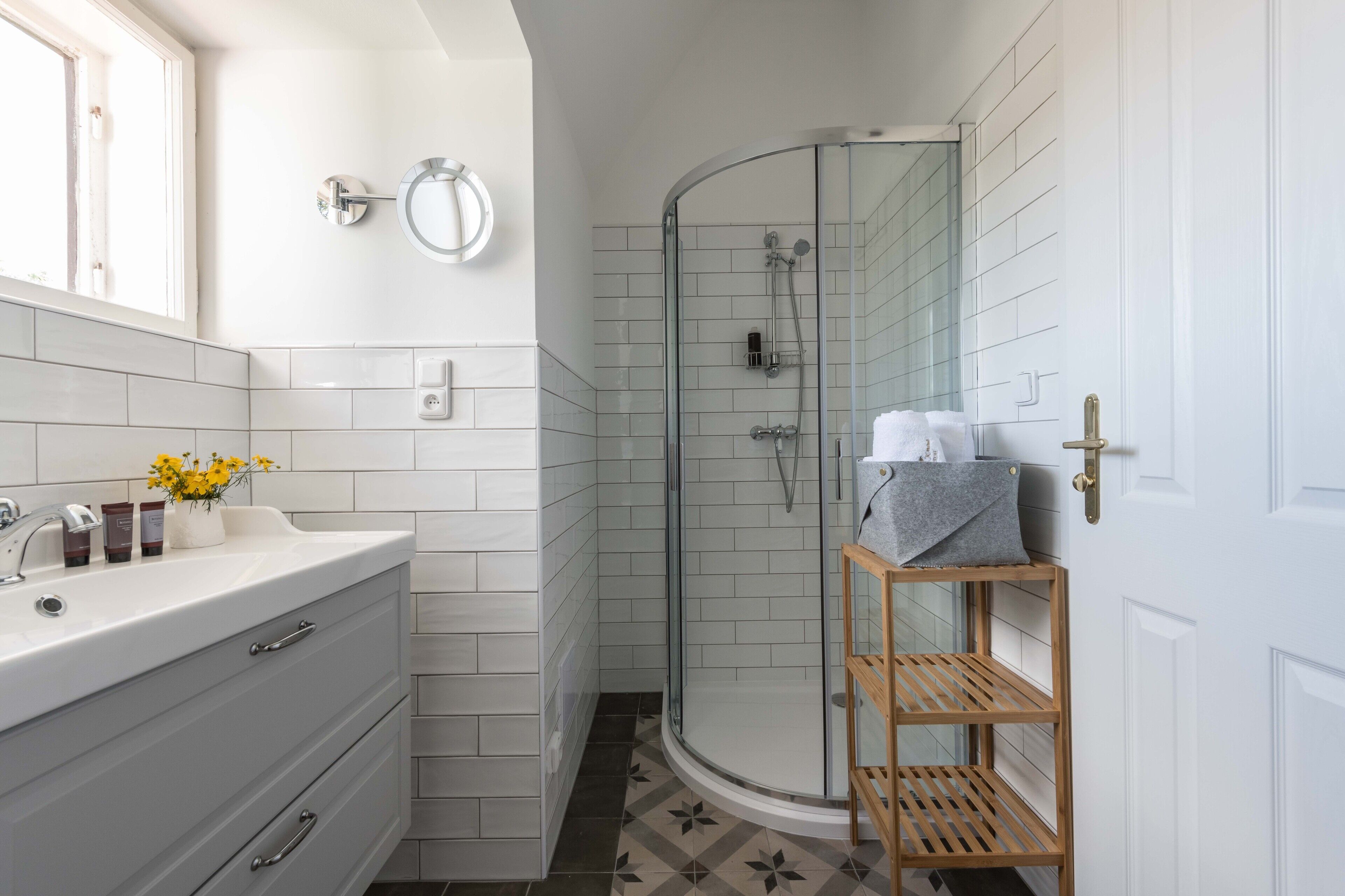 A bathroom with a white vanity, a glass shower enclosure, and a wooden shelf.
