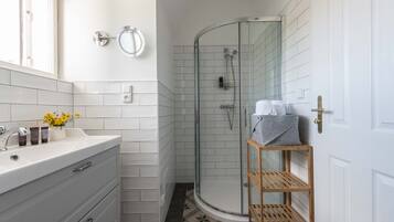 Un baño con tocador blanco, cabina de ducha de vidrio y estante de madera.