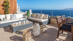 A sunlit outdoor seating area with wicker furniture, a large decorative vase, and a view of the sea. - Home2Book Breathtaking Atlantic Views Apartment (El Rosario)