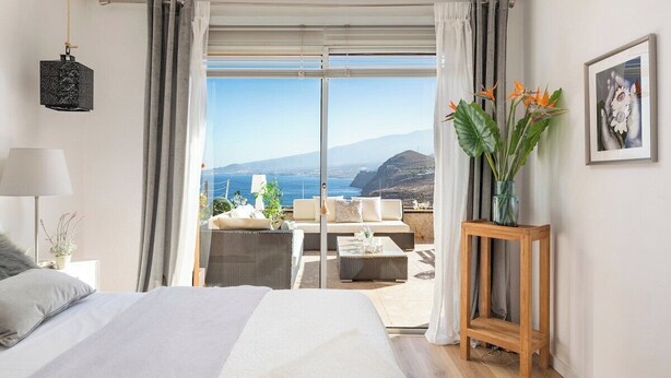 A bedroom with a large bed, a view of the sea, a wooden side table, and a framed picture on the wall. - Home2Book Breathtaking Atlantic Views Apartment (El Rosario)