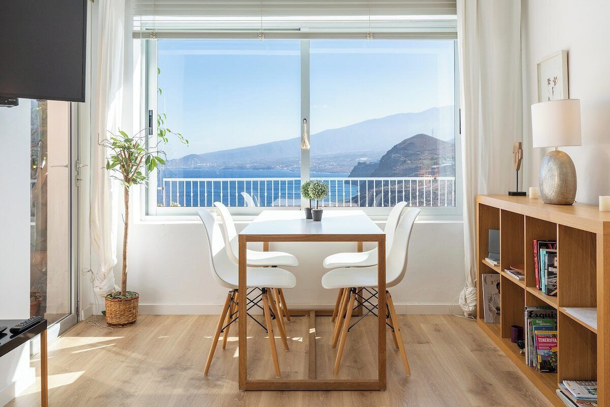 Een moderne kamer met balkon, een eettafel met stoelen, een boekenkast en een potplant.