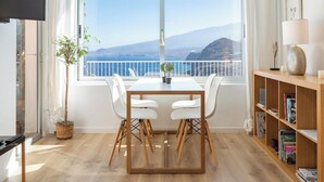 A modern room with a balcony, a dining table with chairs, a bookshelf, and a potted plant. - Home2Book Breathtaking Atlantic Views Apartment (El Rosario)