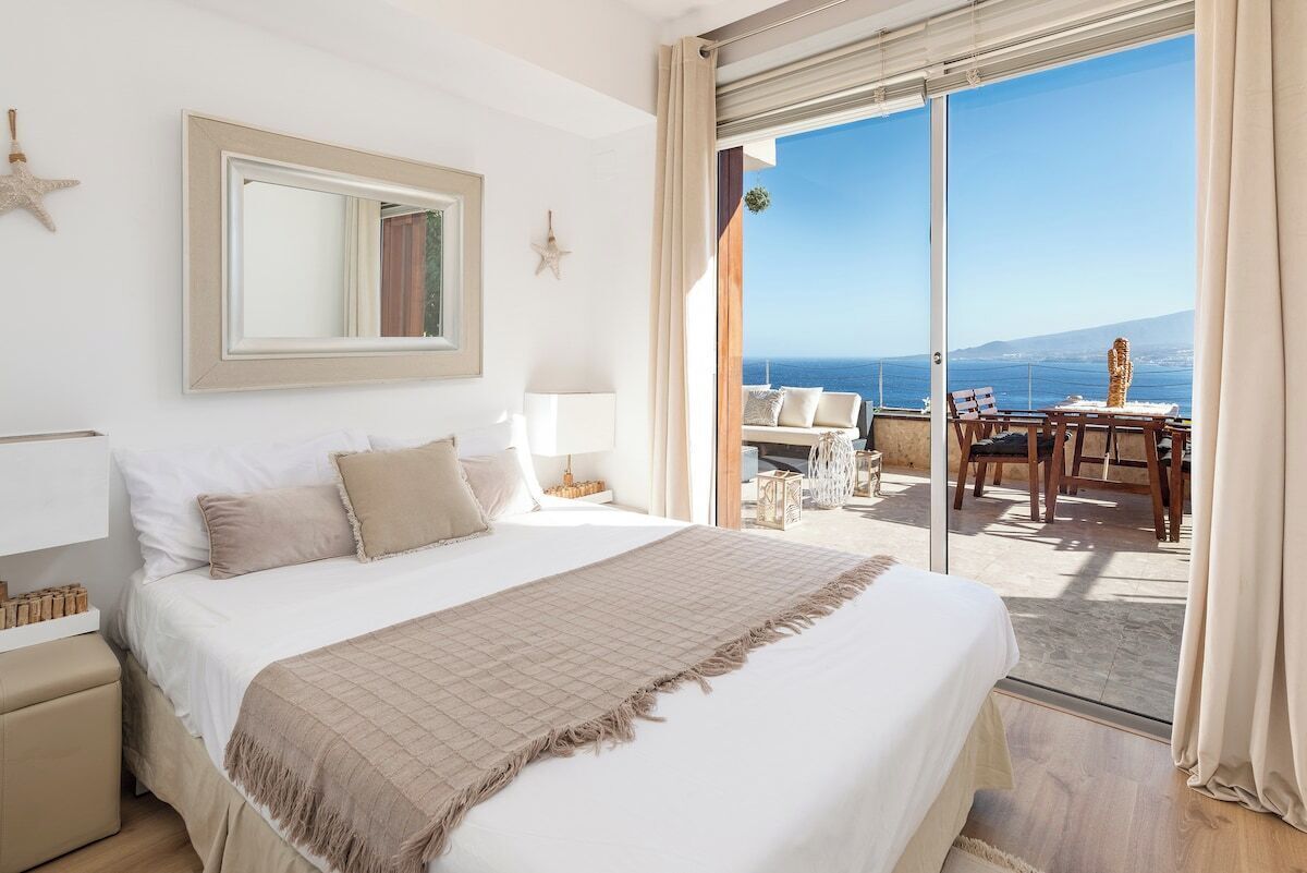 Une chambre d’hôtel avec un grand lit, un balcon avec une table et des chaises, et une vue sur la mer.