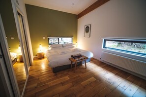 Un dormitorio con una cama grande, una mesita de noche, un ventanal con vistas y un radiador.