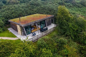 Una cabaña de madera moderna, elevada sobre el terreno, con grandes ventanales, una terraza y un exuberante bosque de fondo.