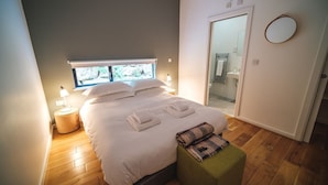 A modern bedroom with a large bed, bedside lamps, a green ottoman, and a view of the bathroom through a glass door. - A yorkshire dale that sleeps 6 guests  in 3 bedrooms (Richmond)