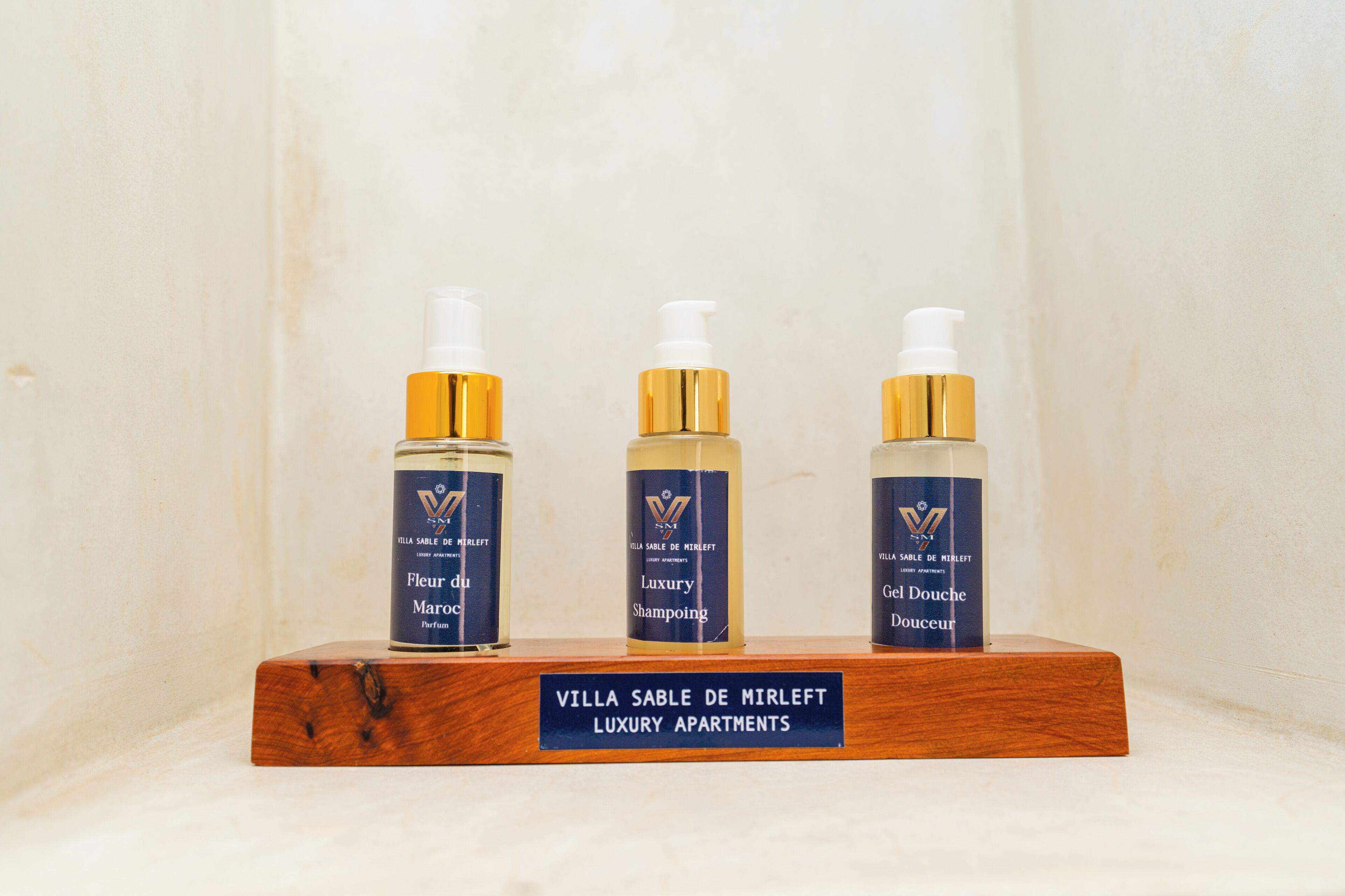 Trois bouteilles de produits de la gamme Villa Sable de Mirleft Luxury Apartments présentées sur un présentoir en bois.