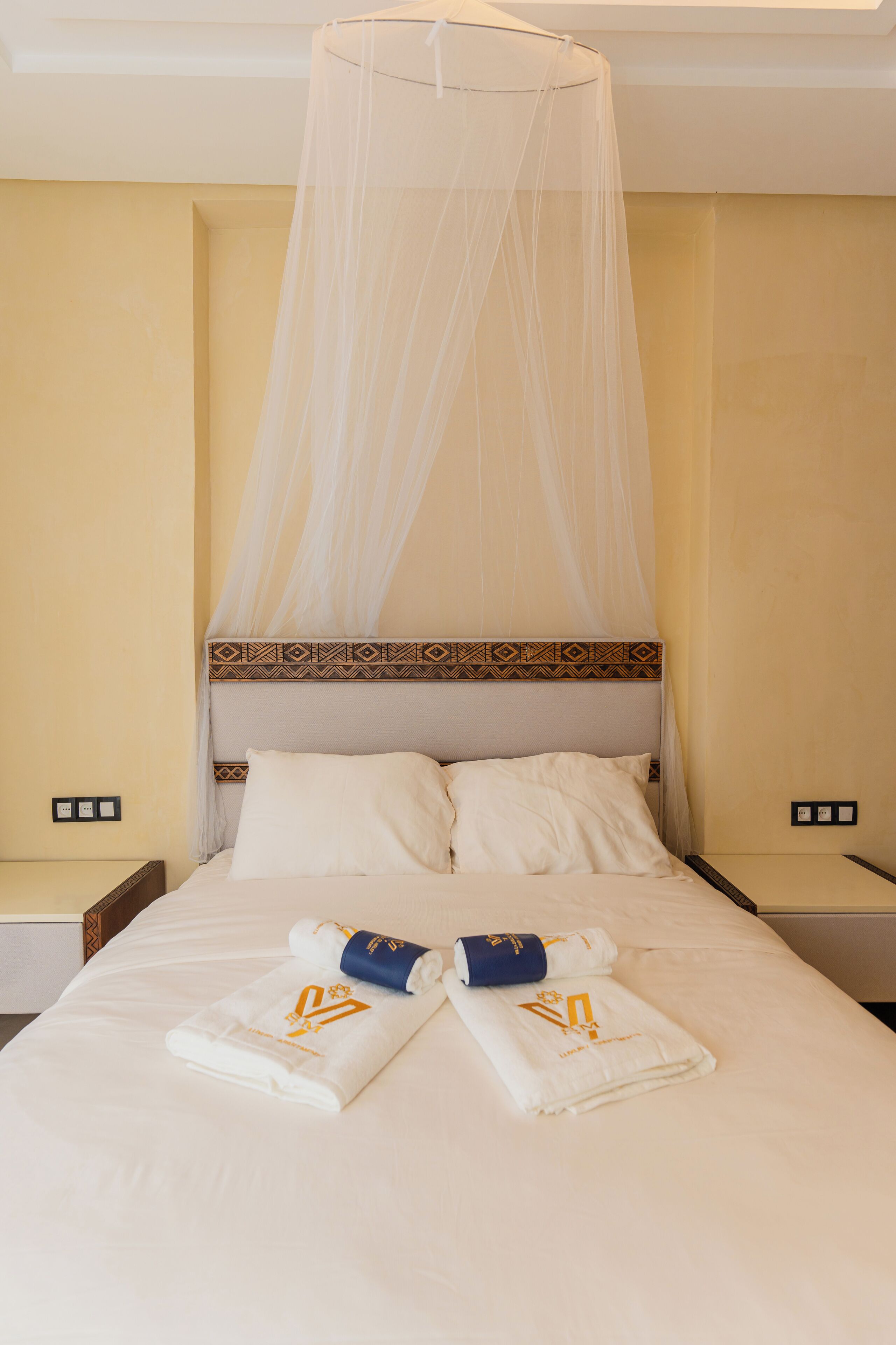 A neatly made bed with a canopy, two pillows, and two towels with a logo.