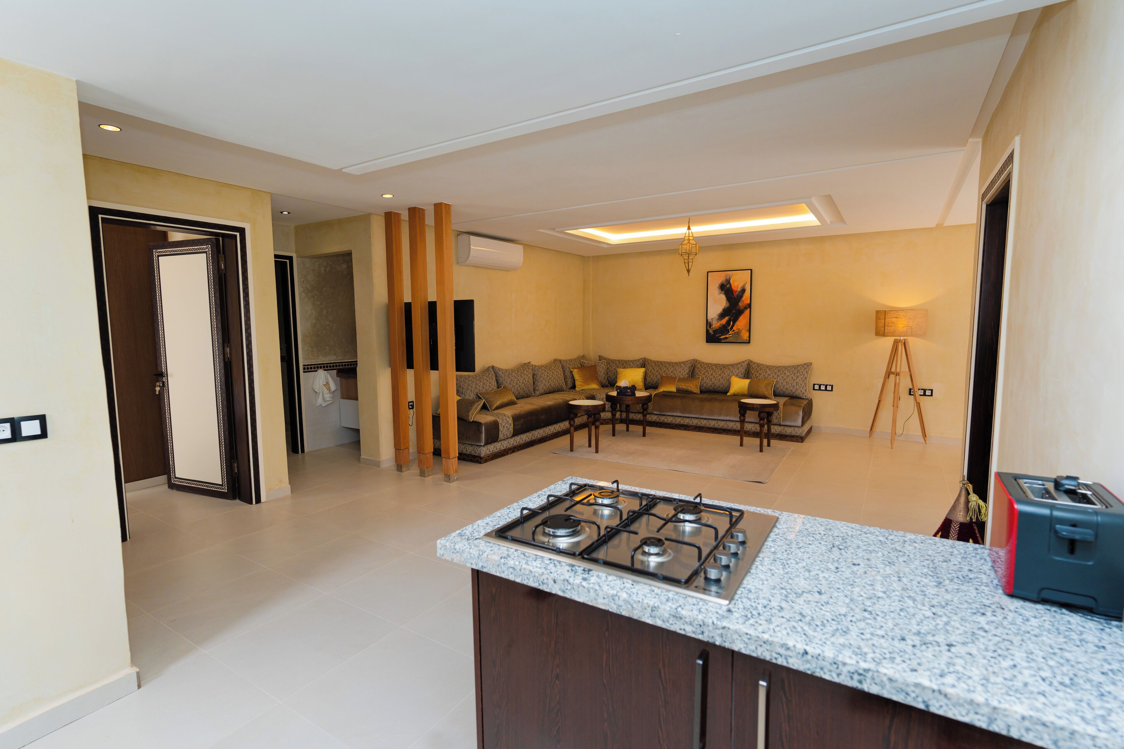 Una cocina moderna con estufa a gas, una zona de comedor con sofá y mesa, y una sala de estar con sofá seccional y un cuadro.
