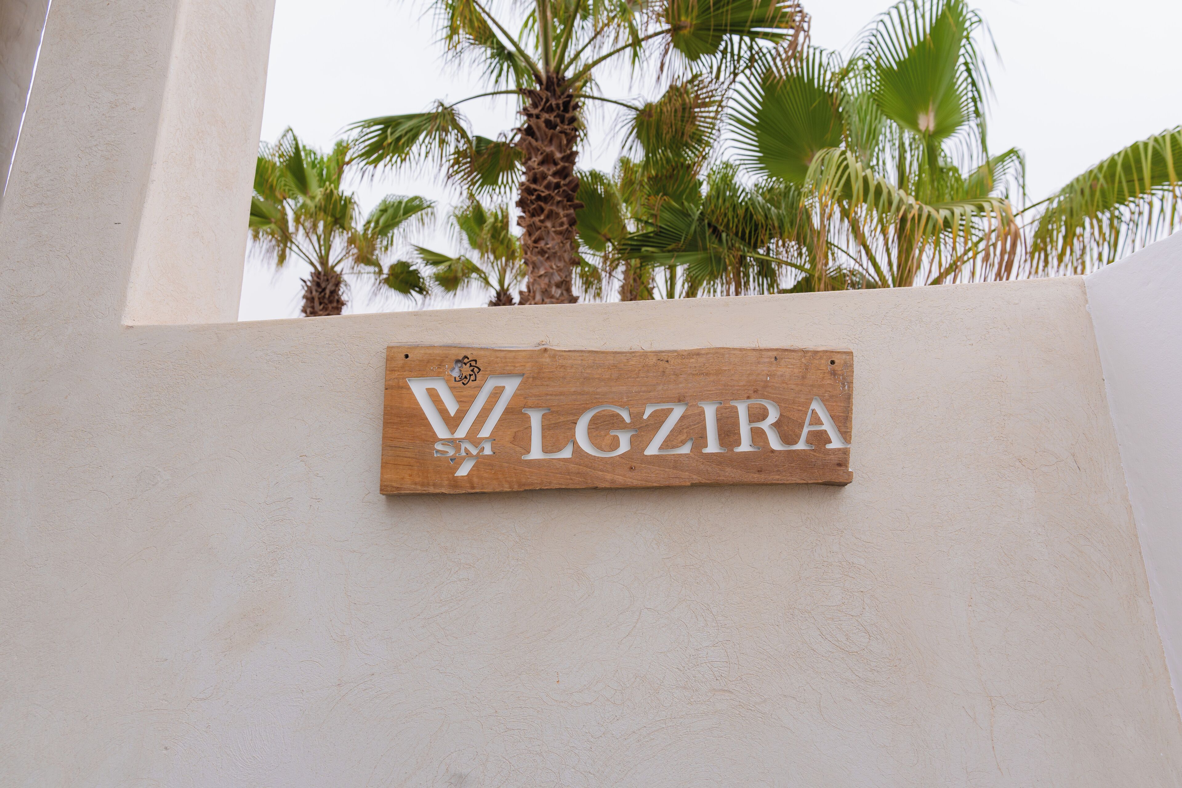 A wooden sign with the text "VGZIRA" and a logo, mounted on a wall.