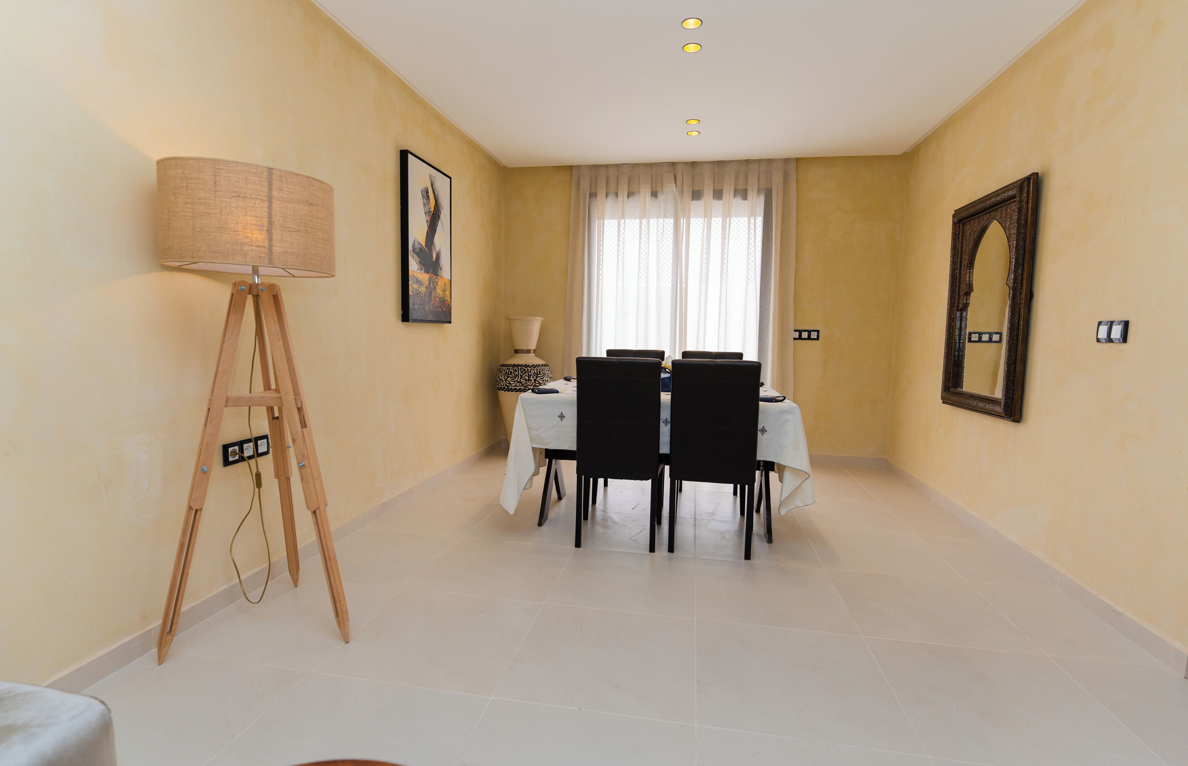 Un coin repas avec une table dressée pour quatre personnes, un lampadaire et un tableau encadré accroché au mur.