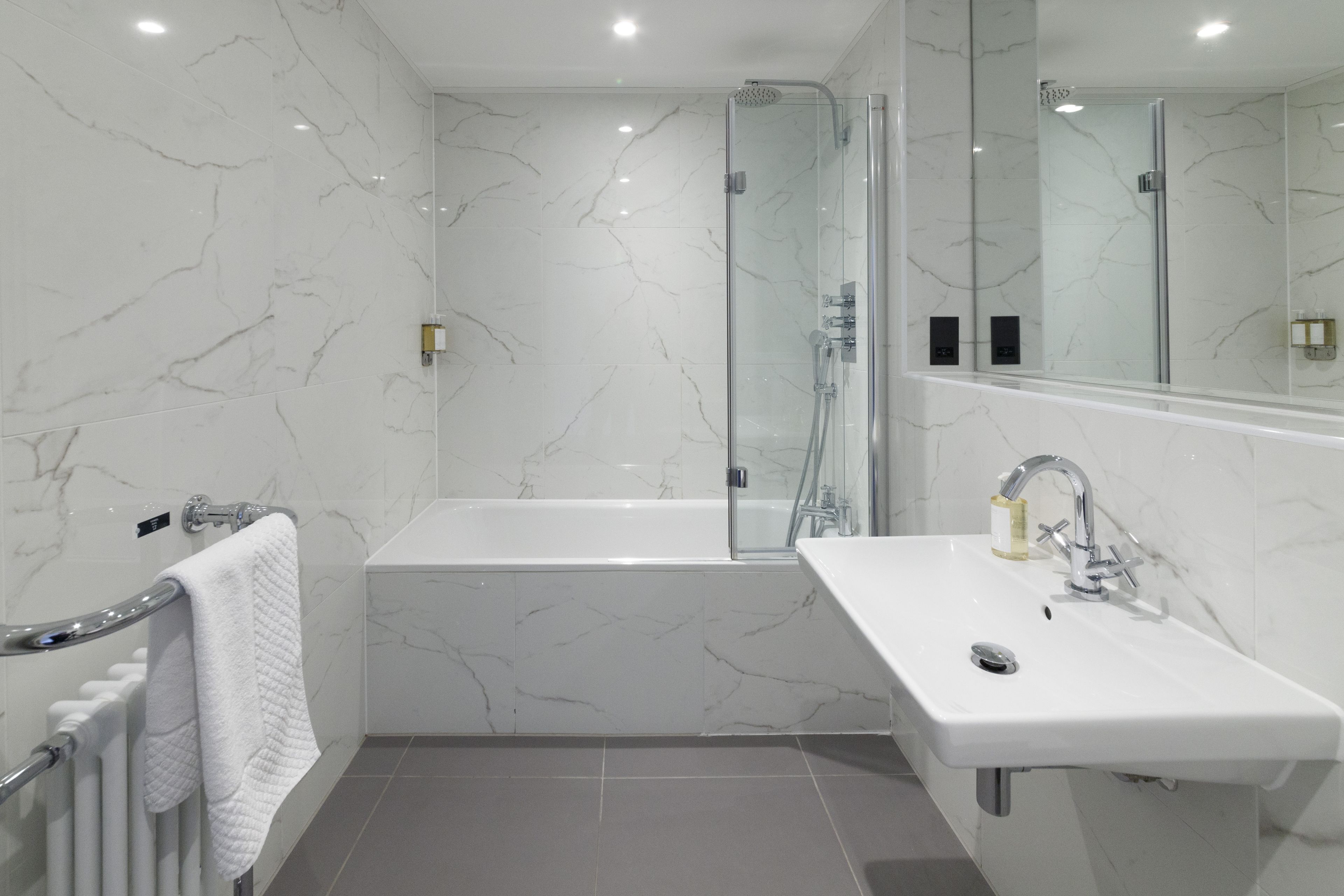 Un bagno moderno con vasca, doccia e lavabo, il tutto con pareti e pavimento in marmo.