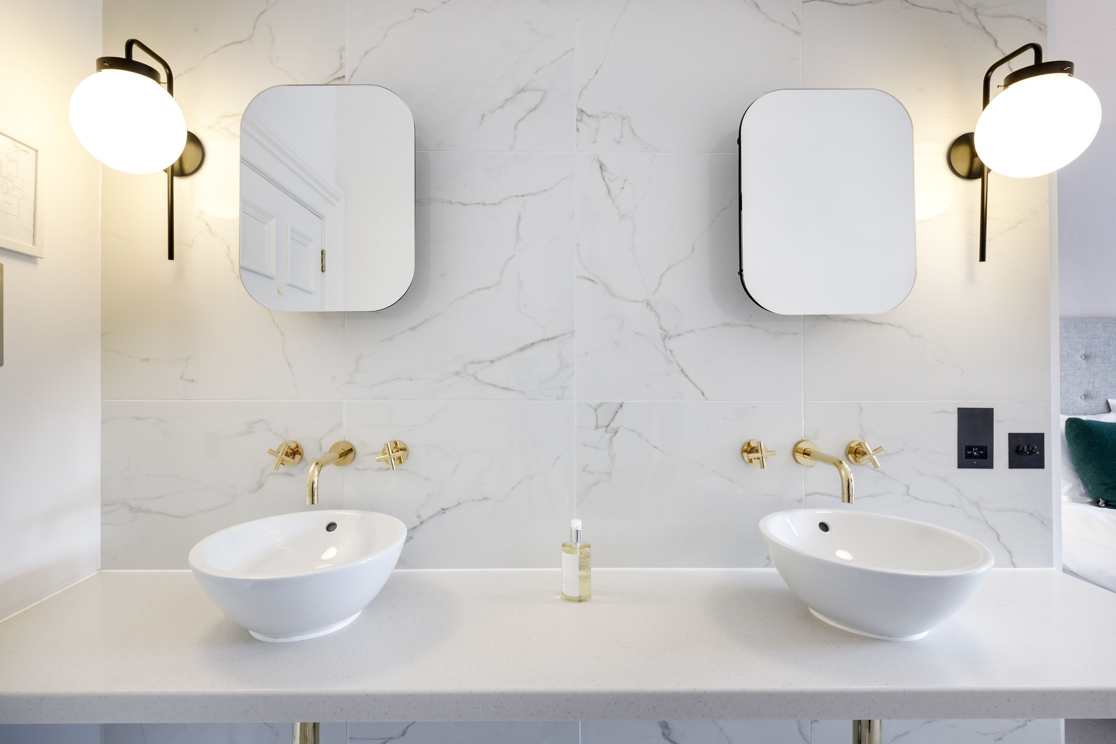 A modern bathroom with two white vessel sinks, gold faucets, and wall-mounted mirrors with round lights.