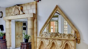 A room with a stone fireplace, a wooden coat rack, and a red sofa. - Empire Hotel (Leicester)