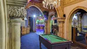 Une table de billard dans une pièce ornée de colonnes en pierre sculptées et d’un lustre.