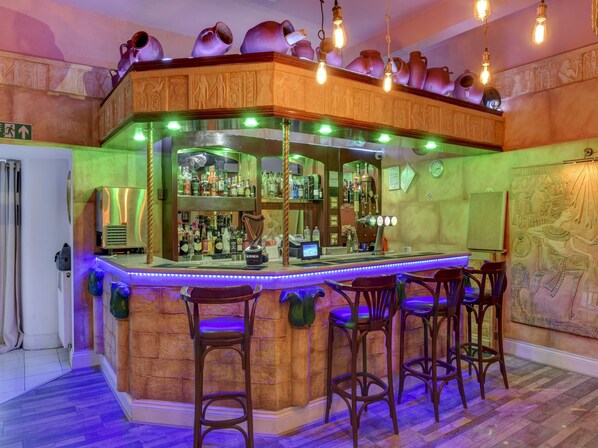 Zona de bar con mostrador, taburetes y una variedad de botellas.