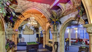 Une salle de billard équipée d’une table de billard, de colonnes décorées et de lustres.