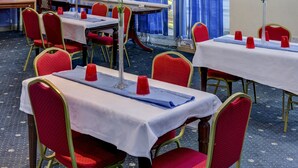 A hotel dining area with tables set for service, red upholstered chairs, and blue curtains in the background. - Empire Hotel (Leicester)