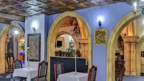 Un espace repas avec des tables et des chaises, un plafond décoré et des œuvres d’art ornant les murs.