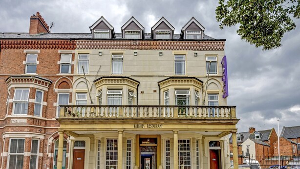 A historic building with a prominent entrance, a balcony, and a sign indicating a bar is open. - Empire Hotel (Leicester)