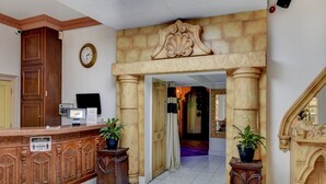 Un espace d’accueil avec un comptoir de réception en bois, une horloge et une arche en pierre menant à un couloir.