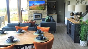 Een moderne woonkamer met een stenen open haard, een televisie en een eethoek met oranje stoelen en een houten tafel.