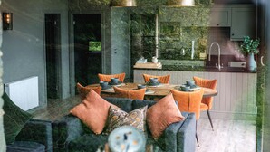Een moderne eetruimte met een ronde tafel, oranje stoelen en een donkere bank met kussens.