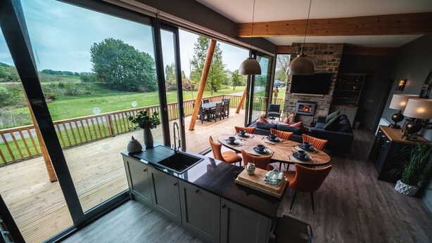 Een moderne keuken met een groot kookeiland, een eethoek met oranje stoelen en uitzicht op de omgeving.
