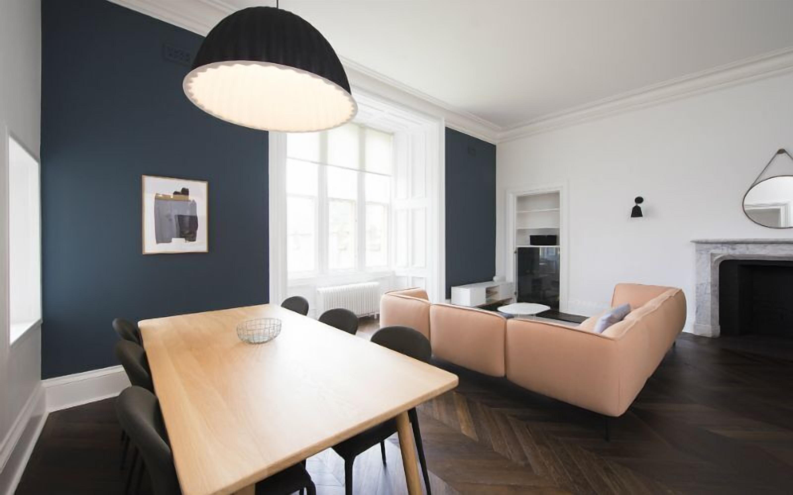 A modern living room with a wooden dining table, a beige sofa, and a black pendant light.