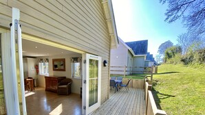A wooden deck with a sliding glass door leading to a dining area with a table and chairs. - Trewhiddle Villa 1 -  a trewhiddle that sleeps 7 guests  in 4 bedrooms (Saint Austell)