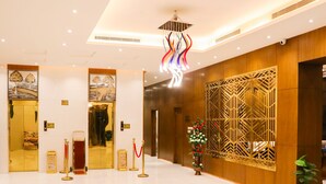 Un vestíbulo espacioso con suelo de baldosas brillantes, una lámpara colgante decorativa y un mostrador de recepción con un panel ornamental.
