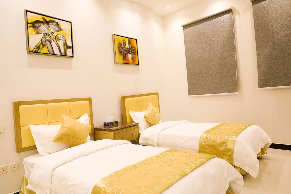 A hotel room with two beds, each with a headboard, a nightstand, and two paintings on the wall.