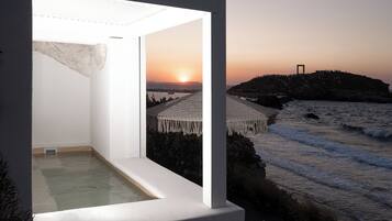 A balcony with a view of the sunset over the sea, a rocky landscape, and a distant building.