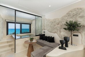 A modern interior with a large window overlooking the sea, a seating area with a view, and a unique textured wall. - Portara Seaside Luxury Suites (Naxos)
