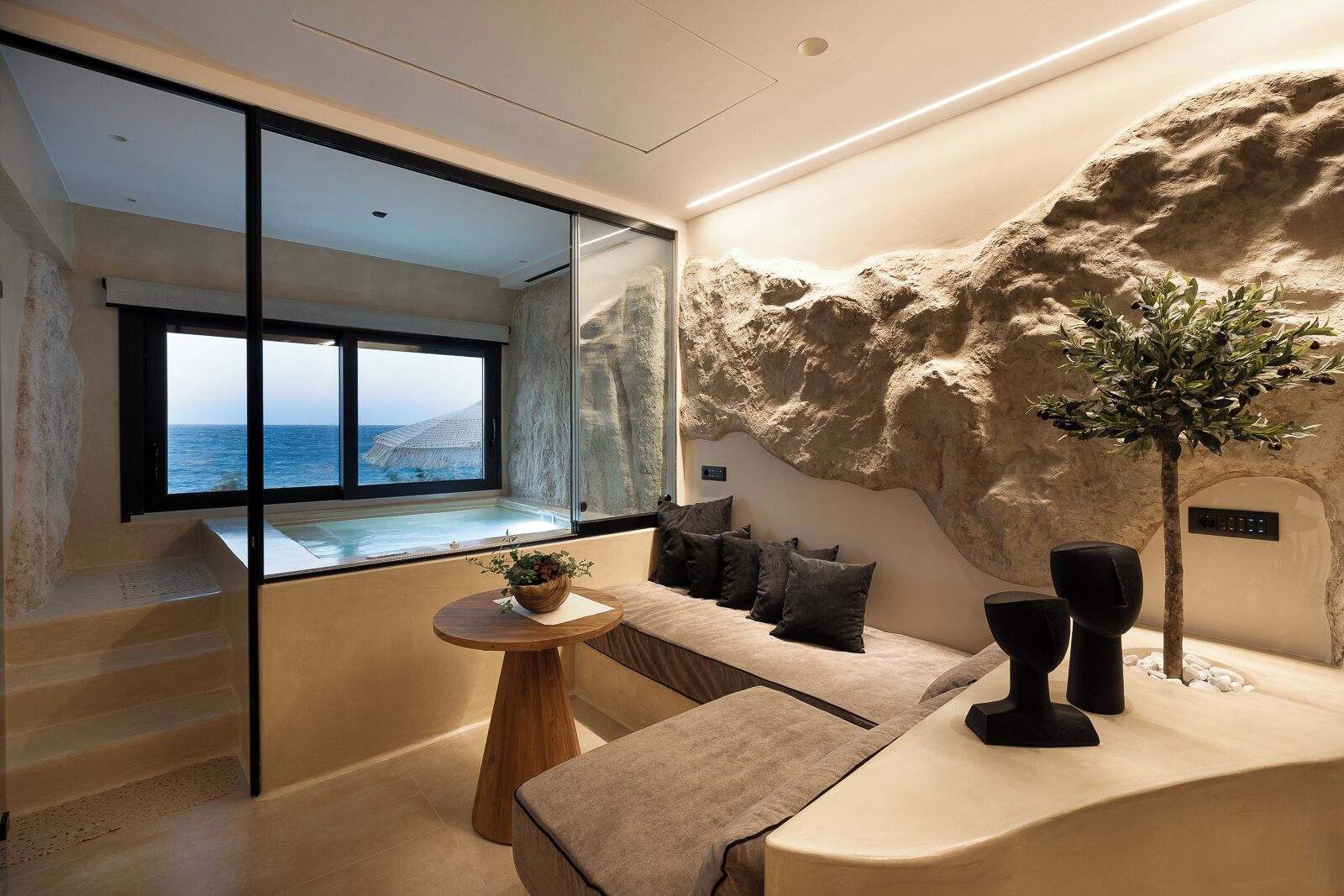 Un interior moderno con vista al mar, una pared de piedra, una zona de estar y una pequeña mesa con una planta.