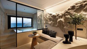 Un interior moderno con vista al mar, una pared de piedra, una zona de estar y una pequeña mesa con una planta.
