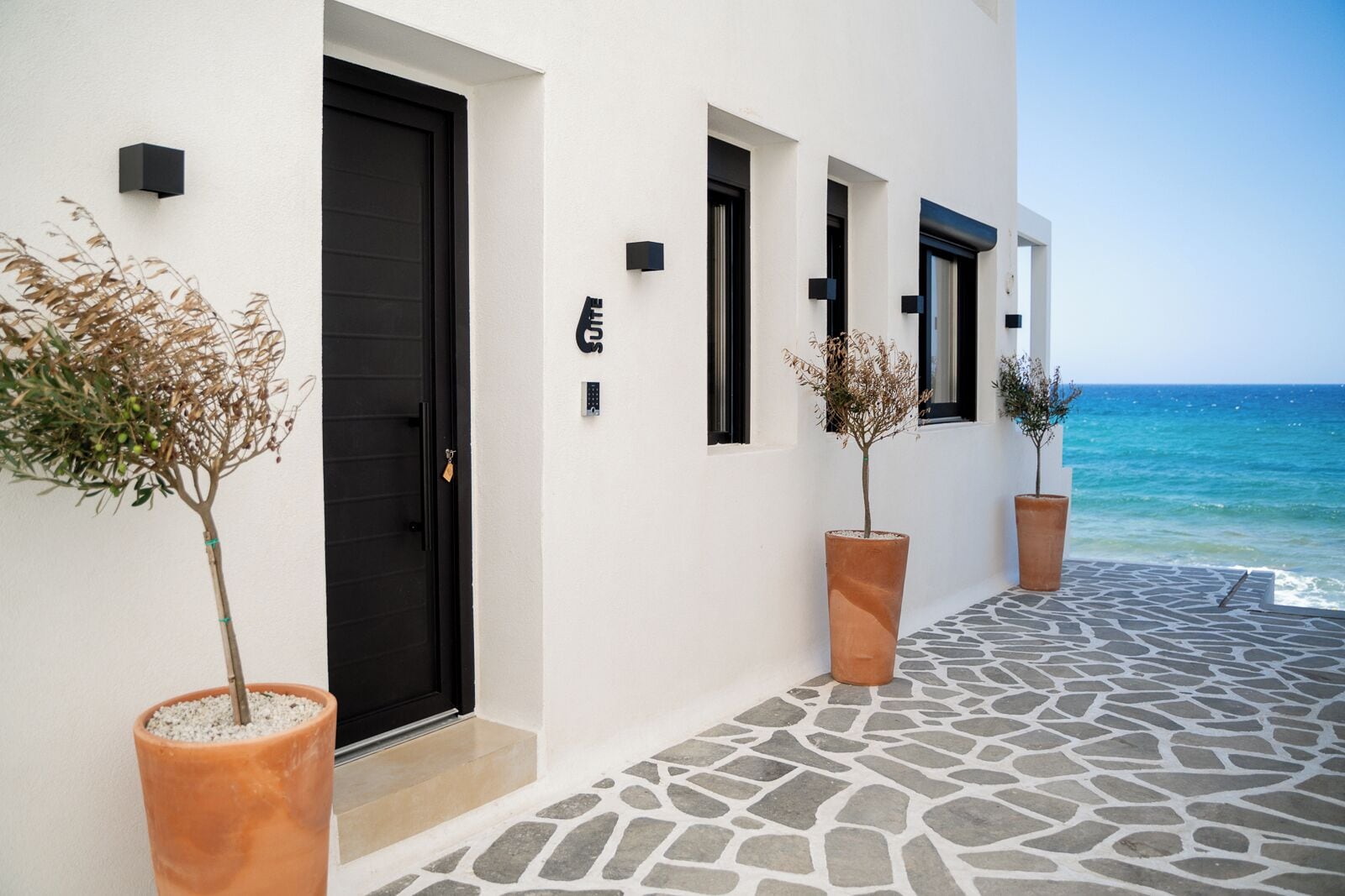 Un hotel costero con entrada empedrada de piedra, puertas de marco negro y plantas en macetas.