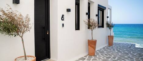 Un hotel costero con entrada empedrada de piedra, puertas de marco negro y plantas en macetas.