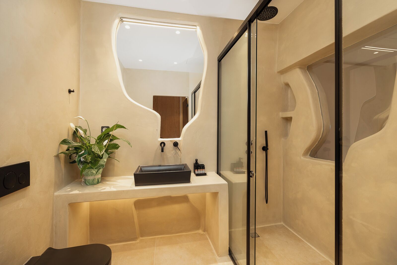 A modern bathroom with a curved mirror, a sink with a plant, and a shower area.