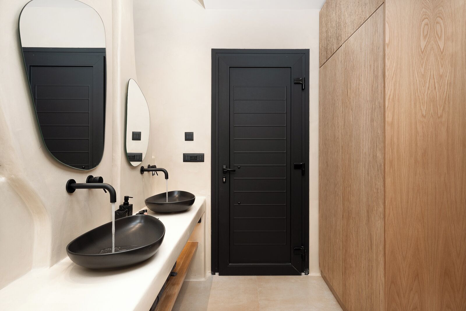 A modern bathroom with a black door, a white sink with a black basin, and a mirror.