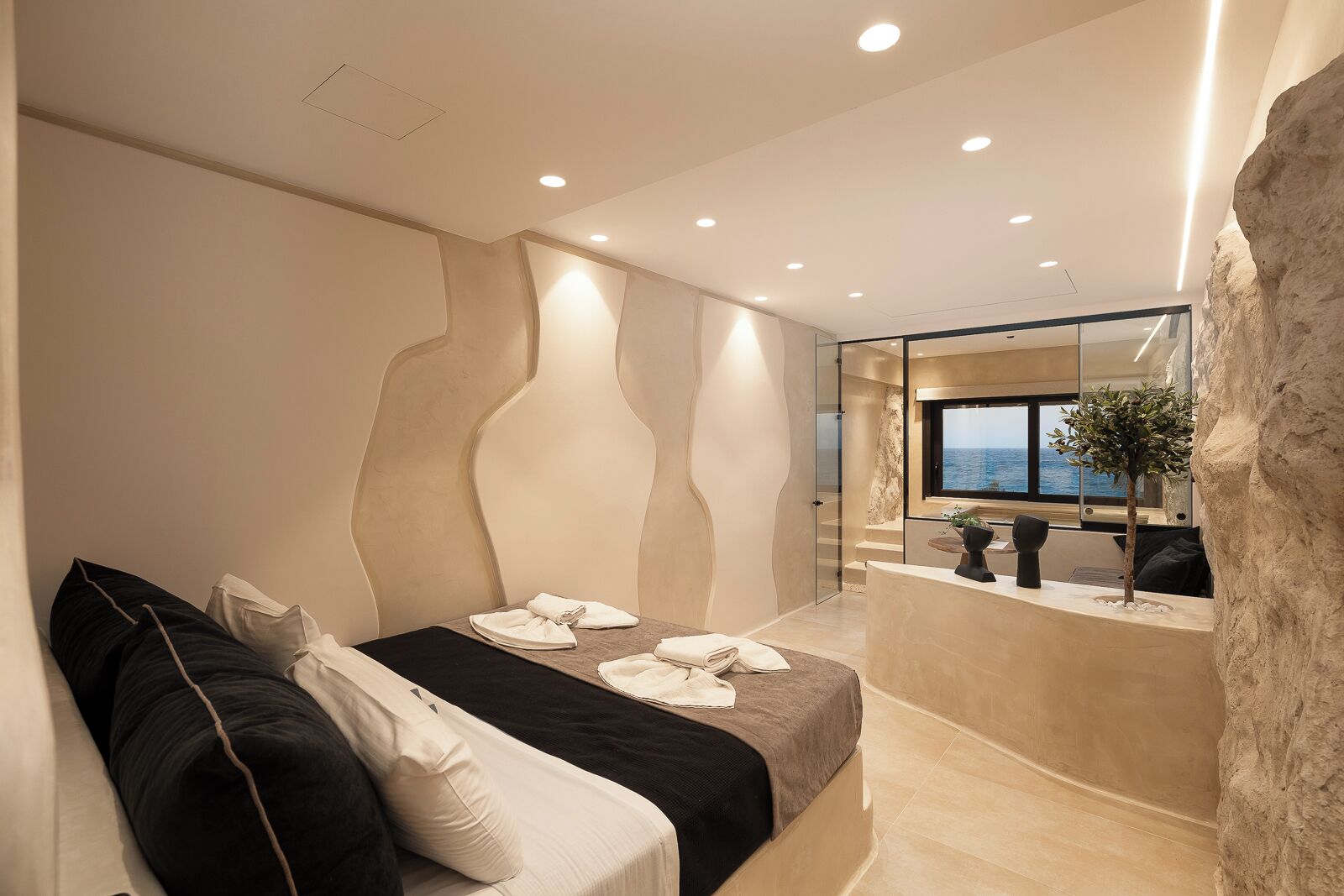 Une chambre d’hôtel moderne dotée d’un lit, d’un coin salon, d’un comptoir de réception et offrant une vue sur la mer.