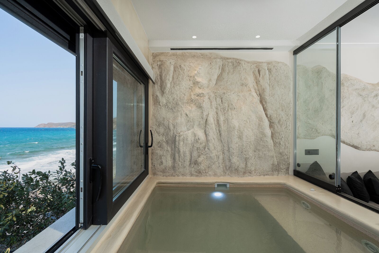 Ein modernes Badezimmer mit einer großen Glasduschtür, Meerblick und einer Steinwand.